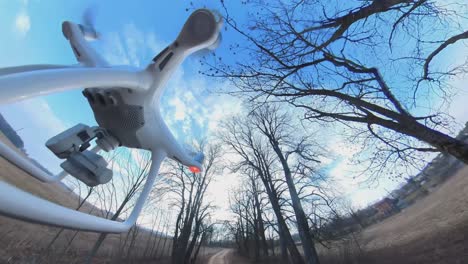 잎이 없는 나무 사이 시골 자갈길 위로 뒤로 날아가는 dji 팬텀 4 쿼드콥터 드론의 클로즈업 측면