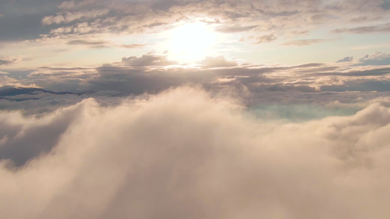 Vista del sole bianco brillante sopra nuvole cumulo e strato bianche e grigie che si muovono nel cielo blu, ripresa aerea.