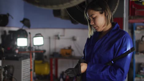 Female-mechanic-holding-led-lamp-wearing-protective-gloves-at-a-car-service-station