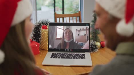 Rückansicht-Eines-Kaukasischen-Paares-Mit-Weihnachtsmützen,-Das-Während-Der-Weihnachtszeit-Einen-Videoanruf-Auf-Dem-Laptop-Führt