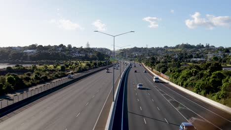 een handheld shot van de auckland snelweg in nieuw-zeeland die wordt doorkruist door verschillende voertuigen op hoge snelheid op een zonnige middag met enkele wolken