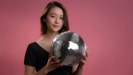 a woman holds a disco ball against a vibrant pink background