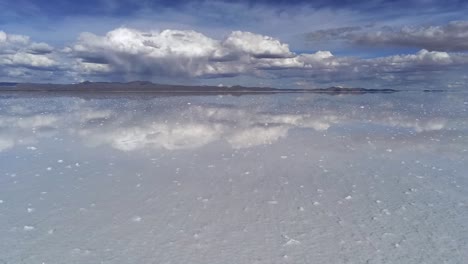 stunning mirror effect low flying drone view over salt flats towards light clouds