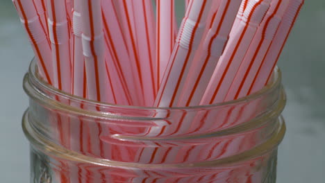 hand grabbing a bunch of single use plastic straws from a glass jar