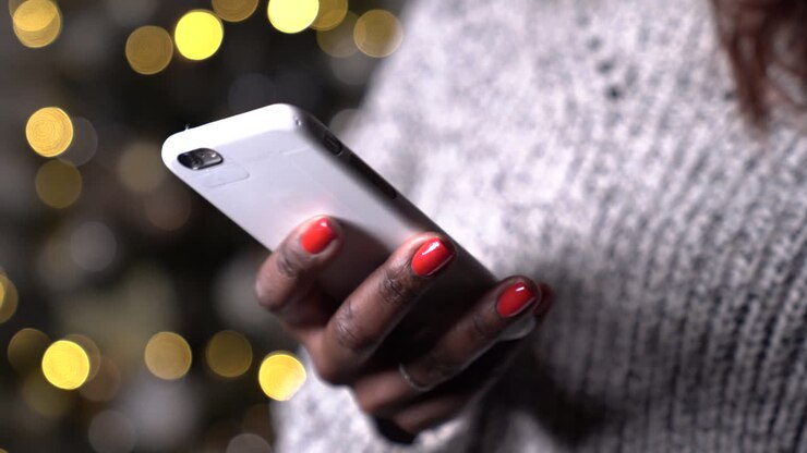 Primo piano di una donna di colore che usa un cellulare, mani che messaggiano con lo smartphone