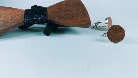 Two-cuffs-and-a-wooden-bowtie-sitting-on-a-white-table,-SLIDE-RIGHT