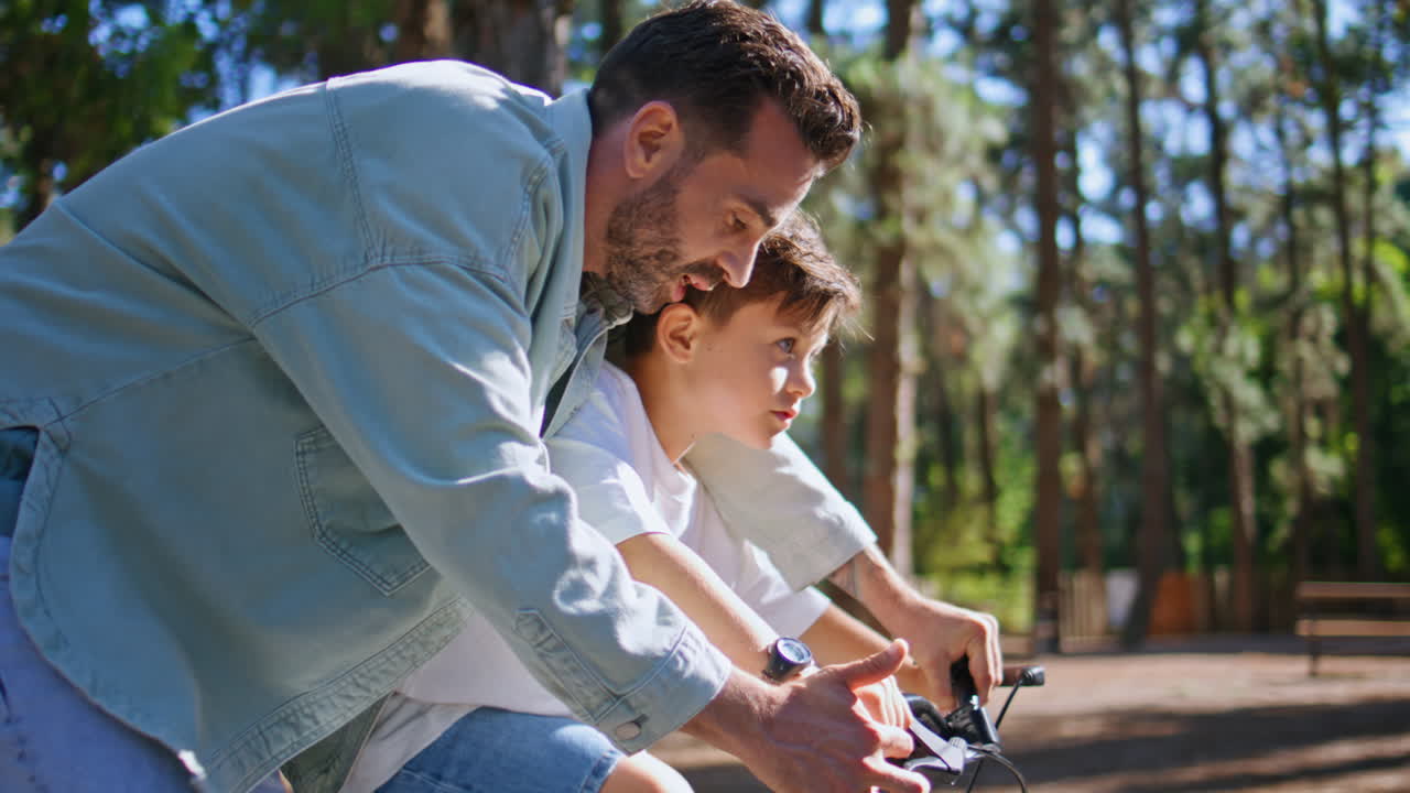 Father teaching son ride bicycle at greenery park closeup. Kid learning sport