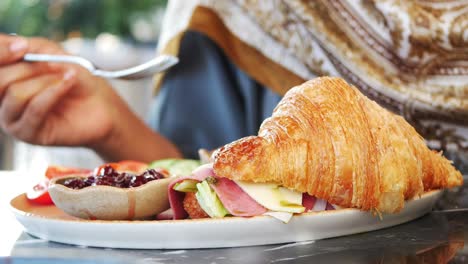 woman eating croissant sandwich in a cafe