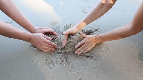 multiple hands shaping sand collaboratively on beach