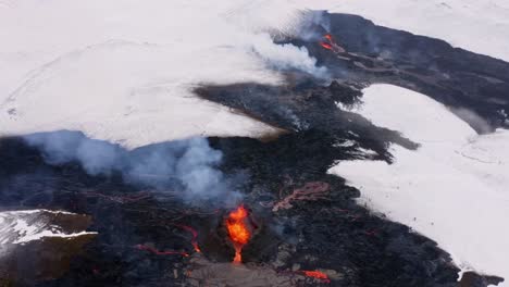 Tomas-Cinematográficas-Tomadas-Con-Un-Dron-En-4k-Capturan-El-Ardiente-Espectáculo-De-La-Lava-En-Medio-De-Campos-Cubiertos-De-Nieve,-Con-Algunas-Secciones-Solidificadas-En-Medio-Del-Paisaje-Invernal.