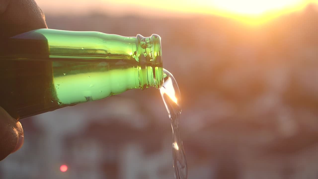 Pouring liquid from a green bottle at sunset