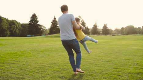 Happy-Father-Holding-Her-Little-Daughter-And-Spinning-Around-On-Meadow-In-The-Park