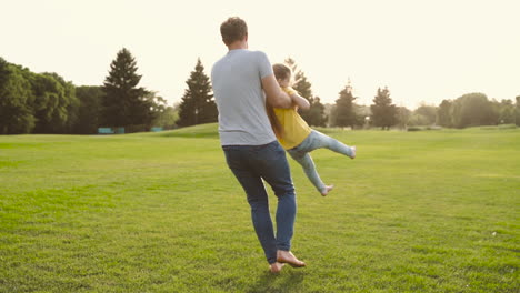 happy father holding her little daughter and spinning around on meadow in the park