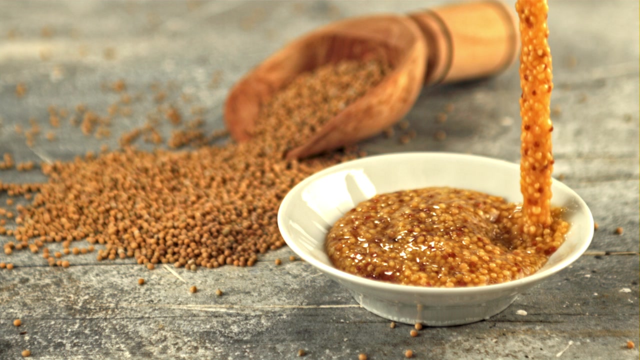 Pouring Whole Grain Mustard into a Small White Bowl