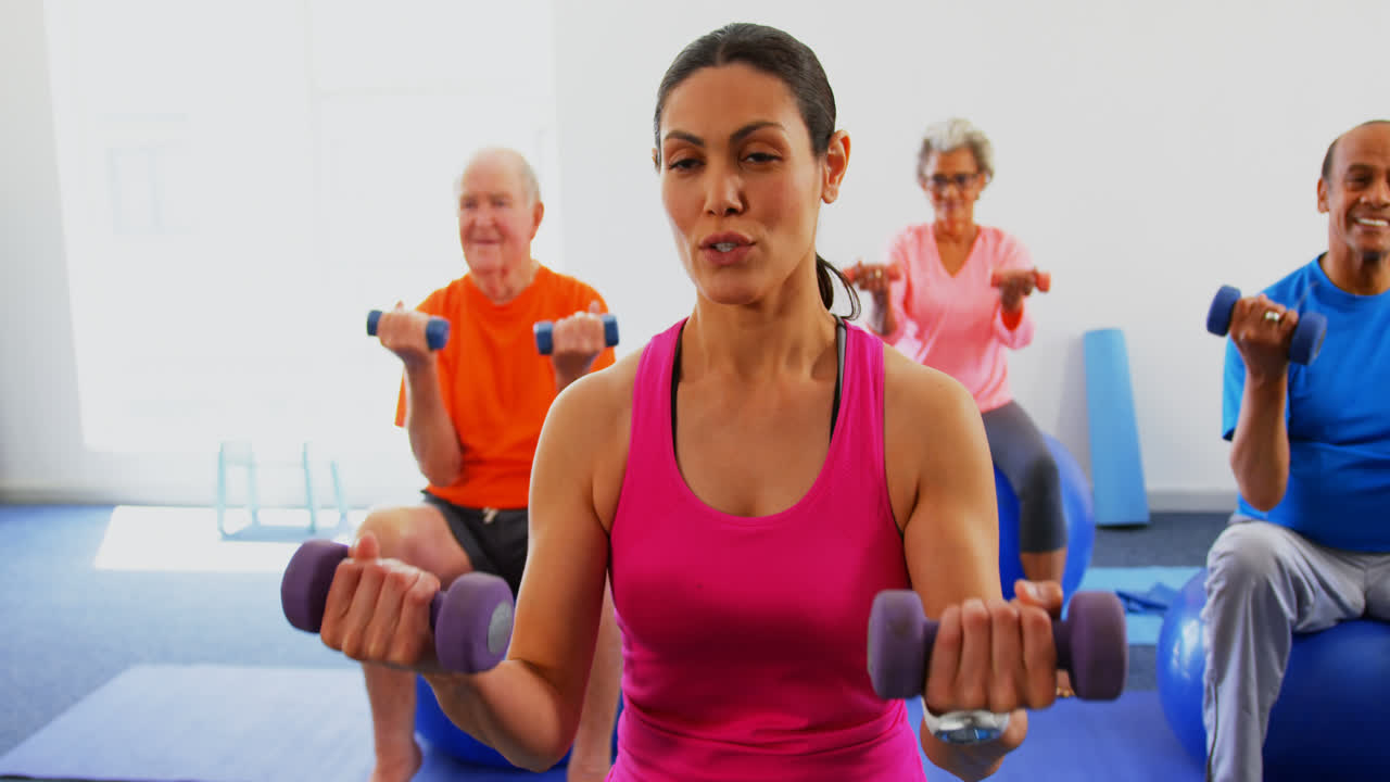 vista frontal de una entrenadora que entrena a personas mayores en ejercicio en un estudio de fitness 4k