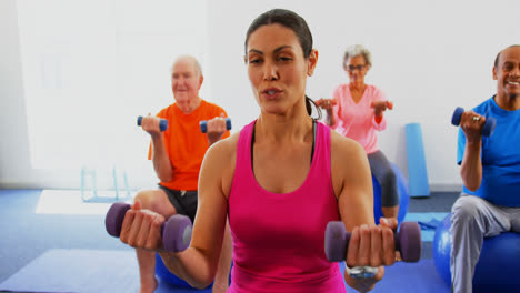 Front-view-of-female-trainer-training-senior-people-in-exercise-at-fitness-studio-4k