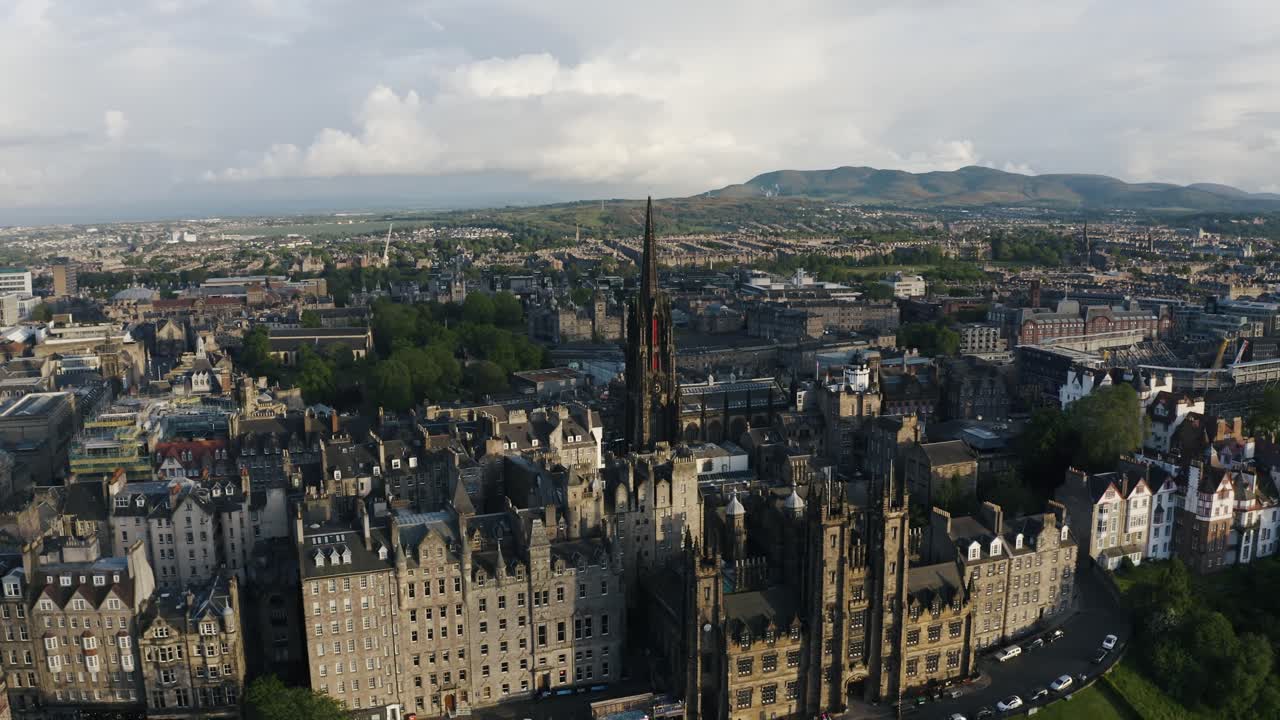 Vista aérea dos edifícios do centro de Edimburgo cercados por uma paisagem rural exuberante, com uma capela alta ao centro.