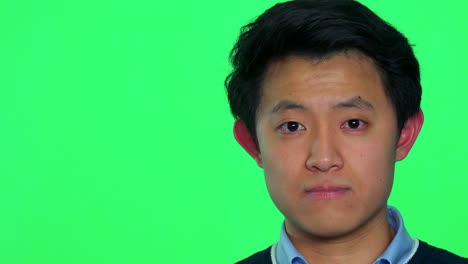 a young asian man looks at the camera - green screen studio - closeup