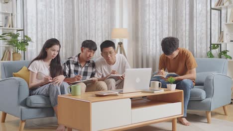 asian teen group studying on a laptop at home, sitting on sofa, taking online course, writing into notebook