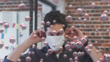 animation of covid 19 cells floating over portrait of caucasian man putting face mask on in office