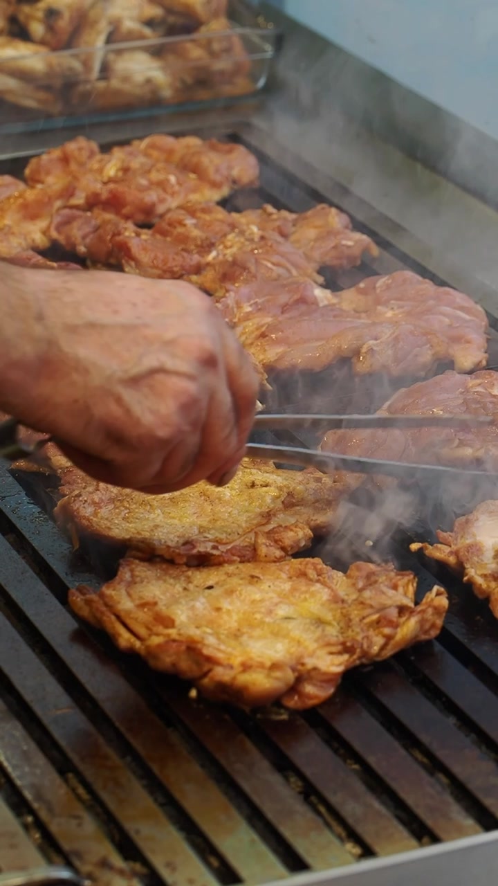 Chef Grilling Marinated Chicken Pieces on a Hot Smoky Griddle