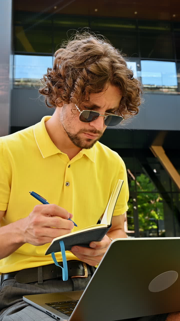 Man in yellow shirt talking standing on a bench and writing in a notebook. Vertical