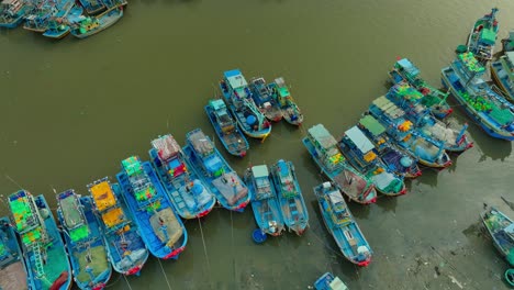 Drone-view-basket-boat-moving-through-fishing-boats-are-nailing-side-by-side-on-the-Ca-Ty-river,-Phan-Thiet-city,-Binh-Thuan-province,-central-Vietnam