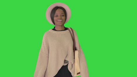 smiling african american woman in knitwear and white hat posing while walking on a green screen, chroma key