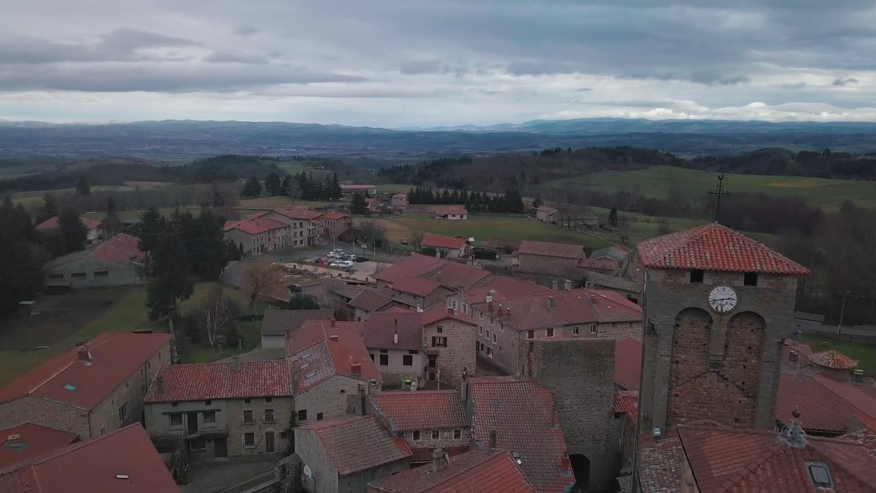 aerial shot over the town of Marols with the fortified church in the foreground and the plaine du Forez in the background on a cloudy day, auvergne rhone alpes region, France