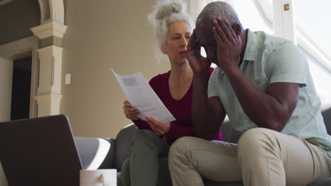 stressed mixed race senior couple discussing finances together in the living room at home