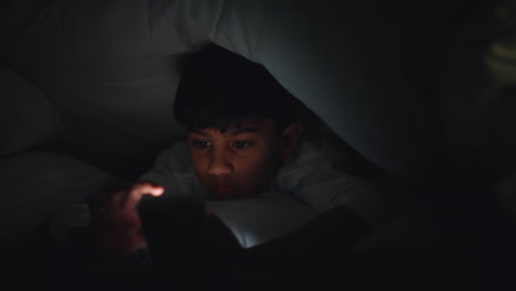 집에서 침실에 있는 어린 소년의 클로즈업은 밤 9시 개나 침대 에서 드폰으로 문자 메시지를 보내고 있다.