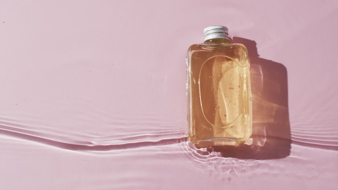 Video di una bottiglia di prodotto di bellezza in acqua con spazio per il testo su sfondo rosa