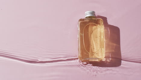 video de una botella de producto de belleza en agua con espacio de copia en fondo rosa