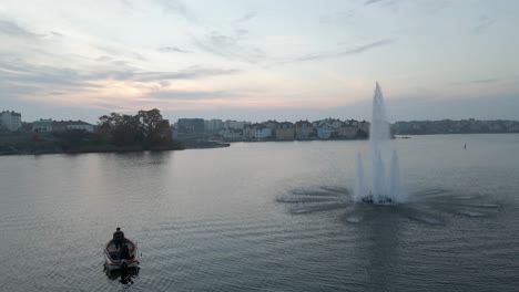 footage of two fishermen sitting in their boat next to the beautiful fountain standing in the middle of the water in the naval city of karlskrona, sweden