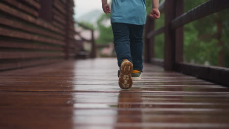 Toddler-Boy-runs-along-wet-veranda-deck-at-cottage-house