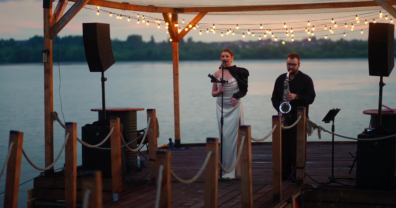 Female Singer and Saxophonist Performing on a Lakeside Pier at Sunset