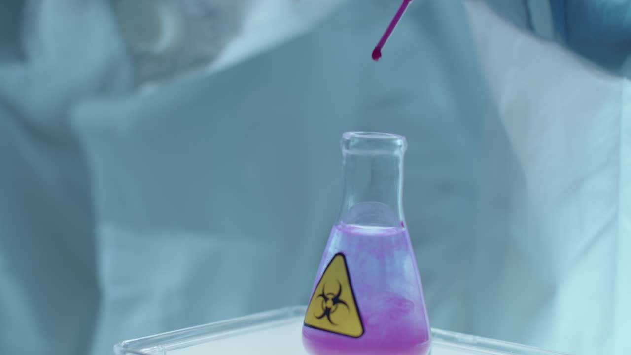 Scientist in Protective Uniform Dripping Liquid in Flask with Biohazard Sticker