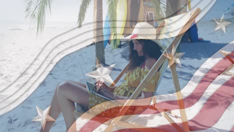 Multiple-stars-on-blue-stripes-against-woman-using-laptop-sitting-on-deck-chair-at-the-beach