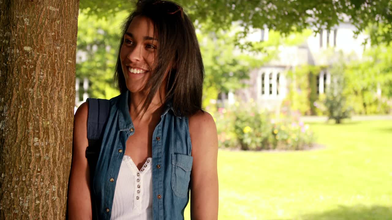 Usmívající se studentka opírající se o strom