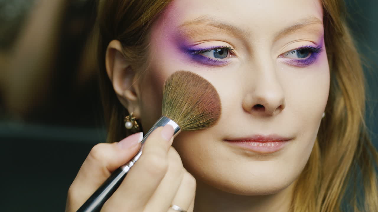 una joven mujer de ojos azules se maquilla en la cara