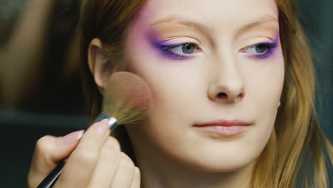 a young blue-eyed woman is applied make-up on her face