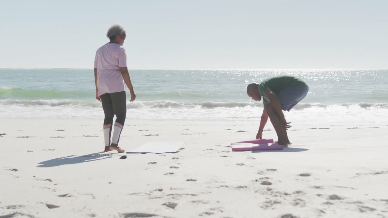 행복한 아프리카계 미국인 부부가 해변에 요가 매트를 놓고 슬로우 모션으로