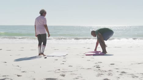 Feliz-Pareja-Afroamericana-De-Edad-Avanzada-Colocando-Esteras-De-Yoga-En-La-Playa,-En-Cámara-Lenta