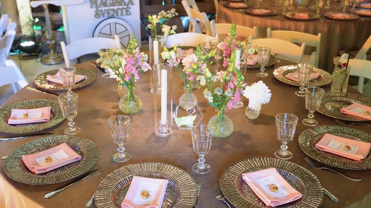 Beautifully decorated round table with ornate plates, blush napkins, delicate glassware, and fresh floral centerpieces under warm indoor lighting, perfect for a stylish event or wedding celebration.