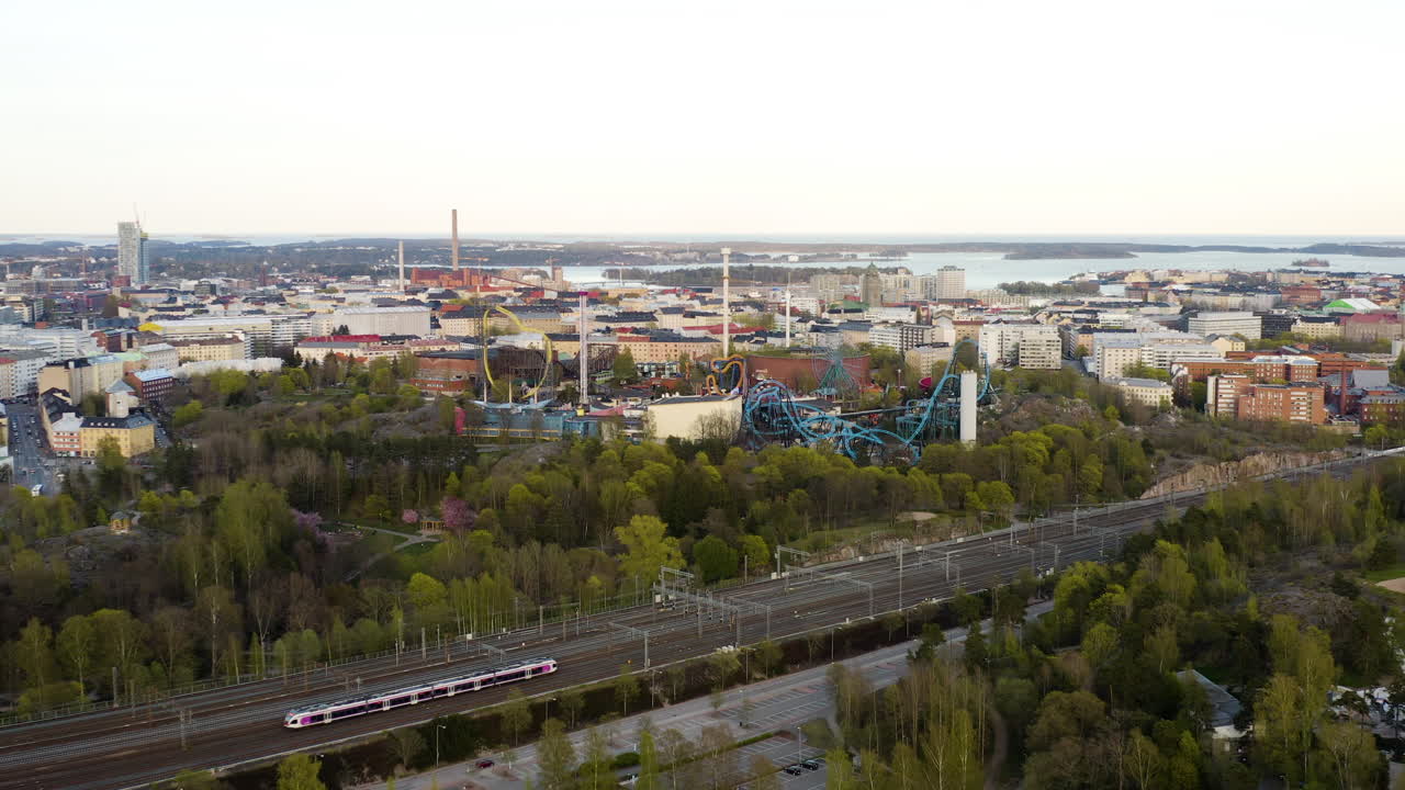 Aerial, drone shot, over a train, towards the Linnanmaki amusement park, sunny, spring day, in Helsinki, Finland