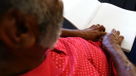 Mid-section-of-blind-senior-man-reading-a-braille-book-at-nursing-home-4k