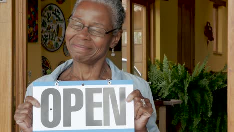 proud older black woman holding an open sign in front of her gallery