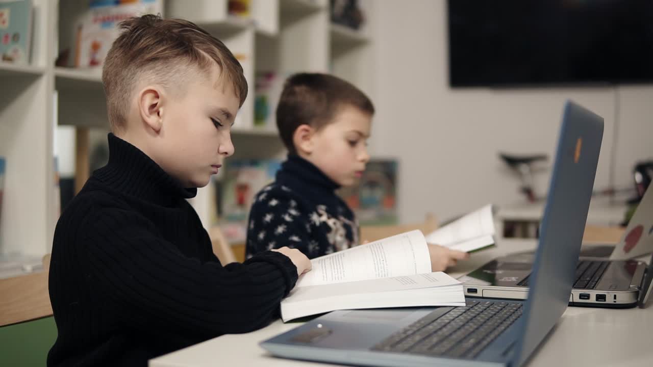 dos niños pequeños leyendo libros en un aula sentados frente a las computadoras portátiles. proceso educativo.