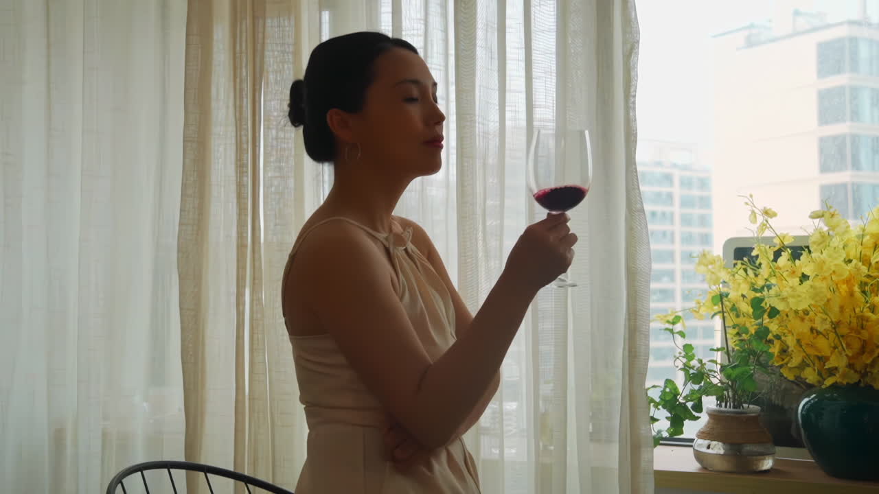 Beautiful woman holding glass, drinking and tasting red wine in winery while enjoying in front of the window