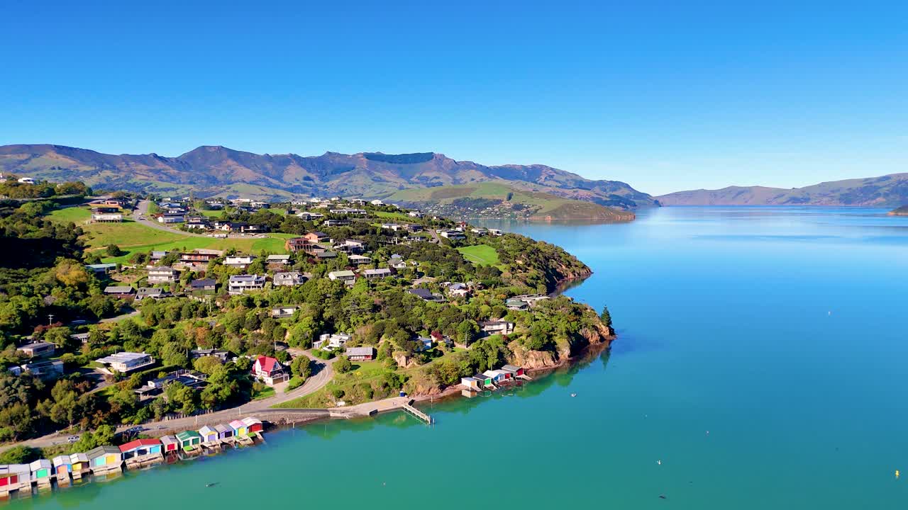 Aerial footage captures Akaroa Harbour's serene waters and lush landscape under clear skies, showcasing the natural beauty of New Zealand
